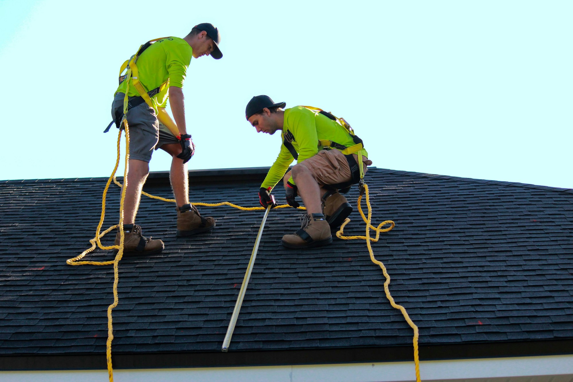 Two roofers installing shingles on a house